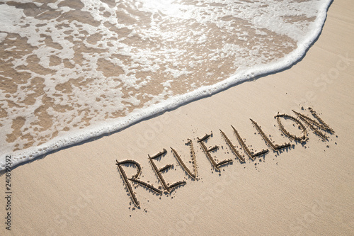 Reveillon, a French word that’s used for New Year’s Eve ceremonies in Brazil, handwritten on Copacabana Beach with a wave in Rio de Janeiro