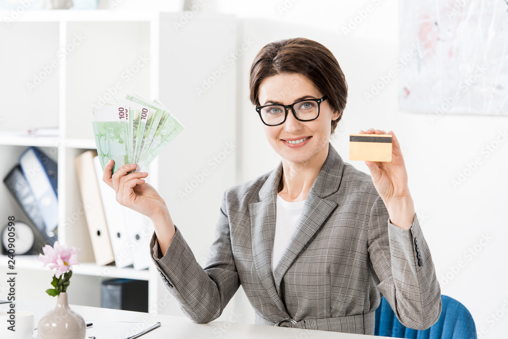 attractive businesswoman showing euro banknotes and credit card in office attractive businesswoman showing euro banknotes and credit card in office
