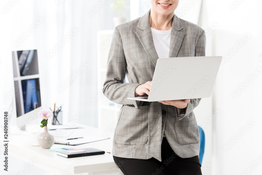 cropped image of smiling businesswoman using laptop in office cropped image of smiling businesswoman using laptop in office