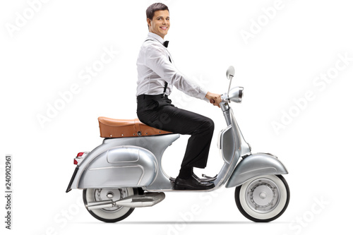 Full length shot of a young man in smart clothes riding a vintage scooter and looking at the camera