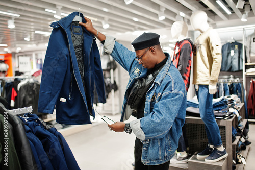 Stylish casual african american man at jeans jacket and black beret at clothes store looking on new jacket.