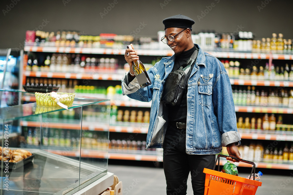 Stylish casual african american man at jeans jacket and black beret holding  basket and looking on bottle of wine, shopping at supermarket. Stock Photo  | Adobe Stock