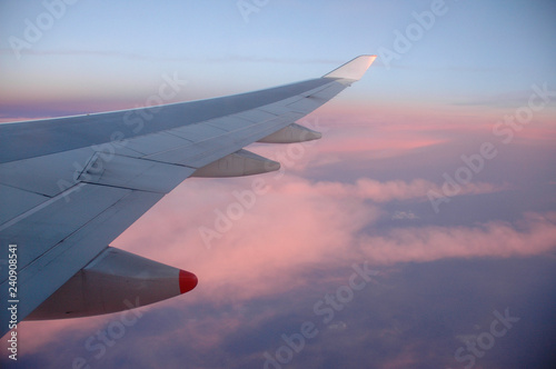 A view from the window of an airplane flying above the clouds during a beautiful sunset. Visible wing of the flying aircraft.