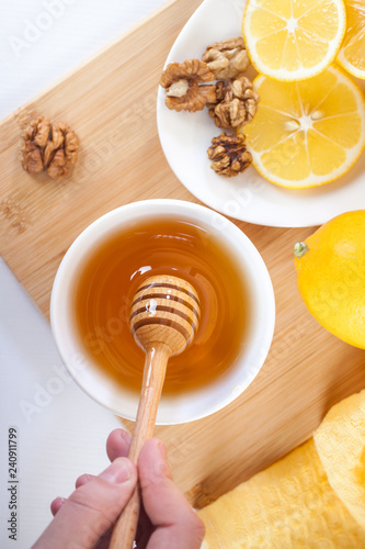 honey in a white ceramic bowl with honey dipper and lemon on a wooden kitchen boar