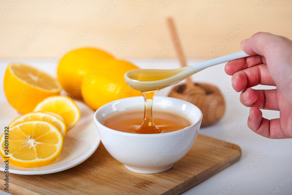honey in a white ceramic bowl with spoon and lemon on a wooden kitchen board honey in a white ceramic bowl with spoon and lemon on a wooden kitchen board