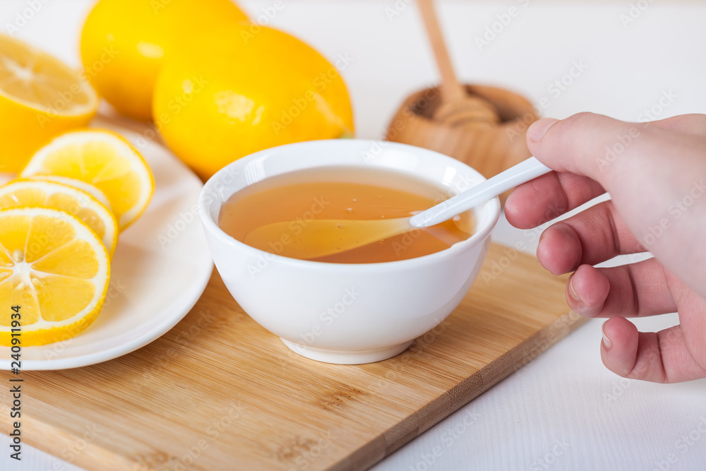 honey in a white ceramic bowl with spoon and lemon on a wooden kitchen board honey in a white ceramic bowl with spoon and lemon on a wooden kitchen board