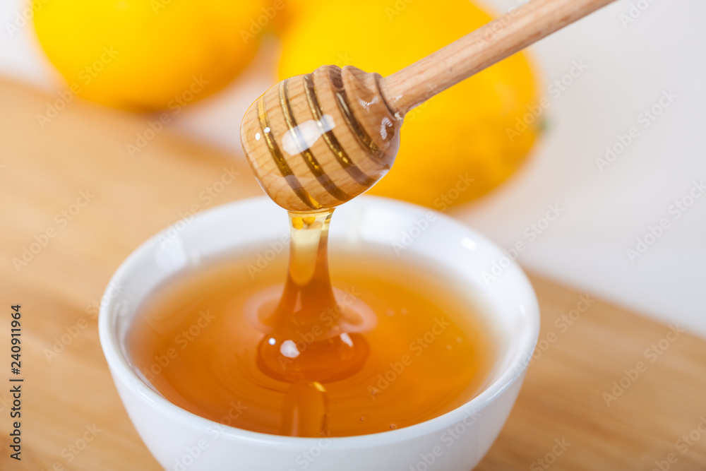 honey in a white ceramic bowl with honey dipper and lemon on a wooden kitchen boar honey in a white ceramic bowl with honey dipper and lemon on a wooden kitchen boar