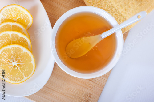 honey in a white ceramic bowl with spoon and lemon on a wooden kitchen board