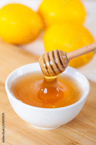 honey in a white ceramic bowl with honey dipper and lemon on a wooden kitchen boar