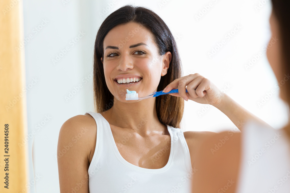 Naklejka premium Pretty young woman brushing her teeth in the bathroom at home.