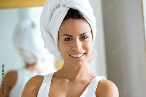 Attractive young woman wrapped a towel around head in her bathroom at home.