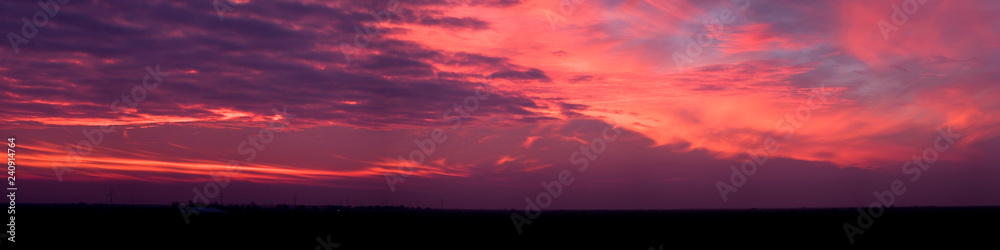 A panorama of dramatic purple pink and orange sunset with wispy clouds.