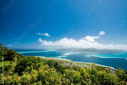 Scenic aerial view on lagoon with blue and turquoise water, green trees, barrier reef, blue sky and white clouds and airport of Raiatea island in French Polynesi