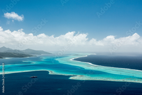 Aerial view on lagoon of Raiatea island in French Polynesia with blue and turquoise water, barrier reef, blue sky, hills with tropical forest and white clouds © Ekaterina Grivet