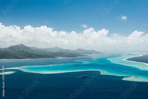 Aerial view on lagoon of Raiatea island in French Polynesia with blue and turquoise water, barrier reef, blue sky, hills with tropical forest and white clouds photo