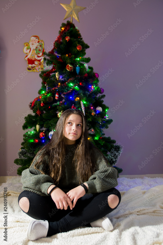 Young girl with christmas tree soft focus low light. Young girl holding sparklers for christmas during winter alone, with beautiful christmass tree bokeh lights in the background
