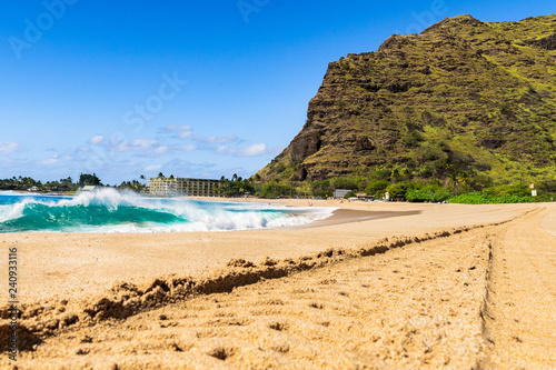 Sunny day at Makaha beach on the west side of the island of Oahu in Hawaii amidst beautiful green mountains with volcanic formation in front of the blue sea photo