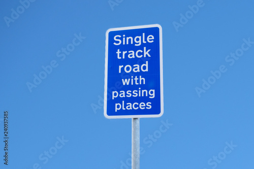 Single track road with passing places sign post against blue sky