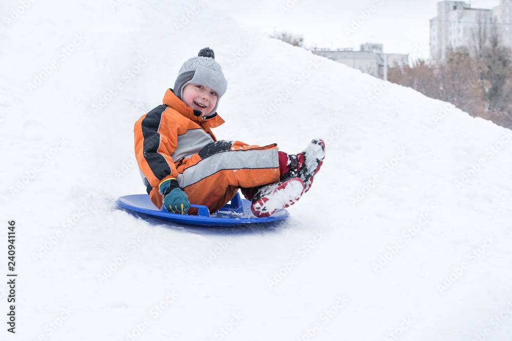Happy laughing small boy slides down the hill on snow saucer. Seasonal concept. Winter day. Happy laughing small boy slides down the hill on snow saucer. Seasonal concept. Winter day.