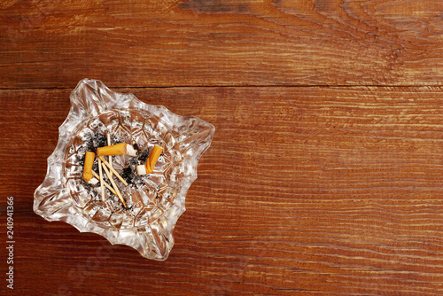 top view of cigarette butts in a glass ashtray on a wooden background with copy space photo