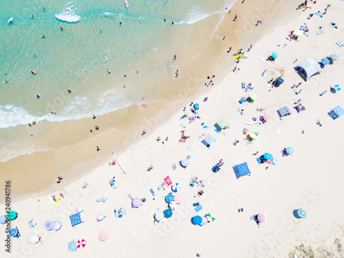 An aerial view of people on the beach with blue water on hot summer's day