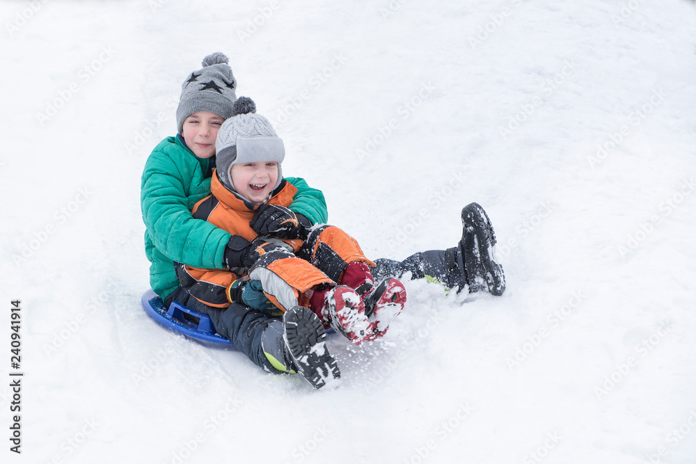 Two joyful boys slides down the hill on snow saucer. Brotherly friendship. Winter day Two joyful boys slides down the hill on snow saucer. Brotherly friendship. Winter day