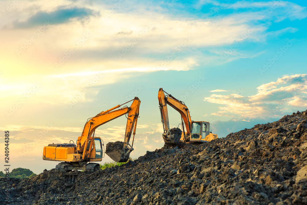 Two excavators work on construction site at sunset