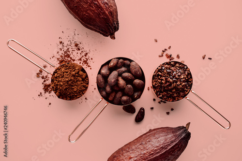 Rose gold measuring cups of cocoa beans, cacao nips, cocoa powder and cocoa pods on a pink background, flat lay healthy food concept photo