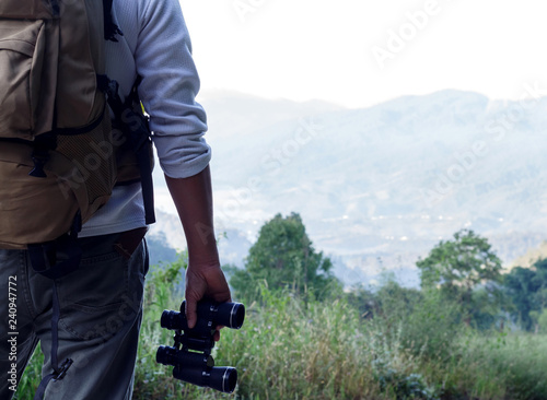 Young man with backpack and holding a binoculars standing on top of mountain