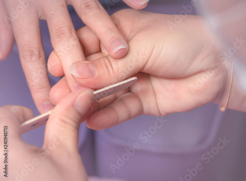 Asian woman receiving fingernail manicure service by professional  manicurist at nail salon. Beautician file nail manicure at nail and spa salon. Hand care and fingernail treatment at nail salon.