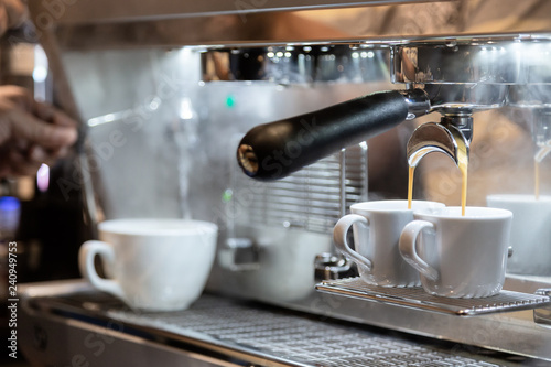 Close-up of espresso pouring from coffee machine with steam in background at coffee shop