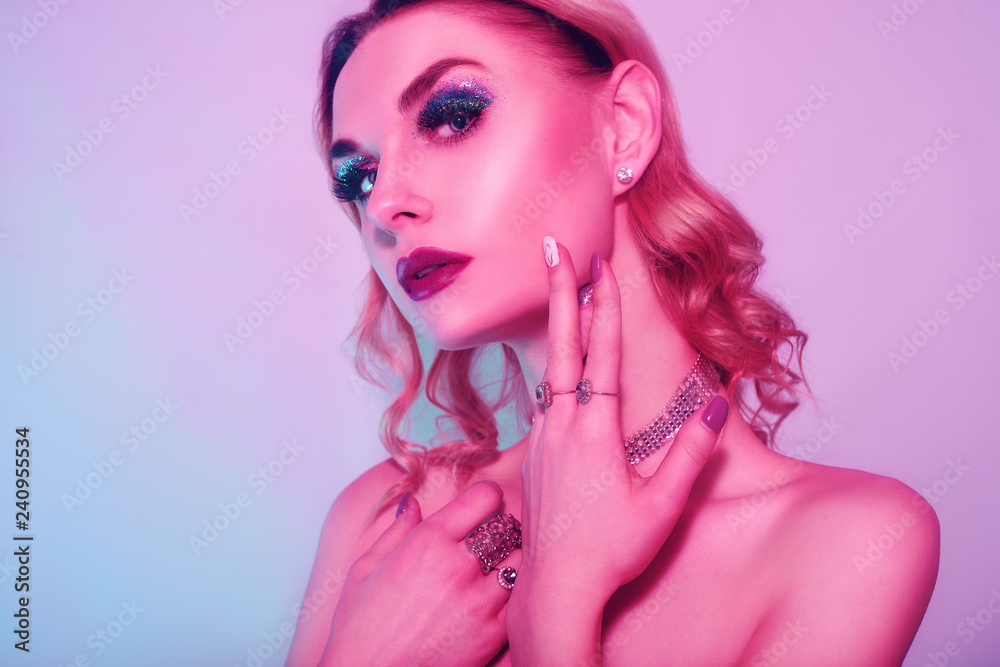 Naklejka premium Beautiful woman in a necklace, earrings and ring. Model in jewelry, diamonds. Fashion neon portrait of young beautiful girl with jewelry. Blond girl with cerly hair and red lips. Perfect make-up. 