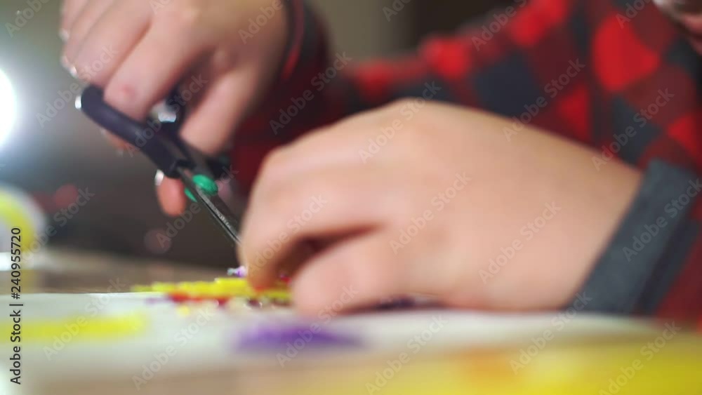 A teenager boy cuts off excess plastic with scissors. He creates a 3D figure from plastic.