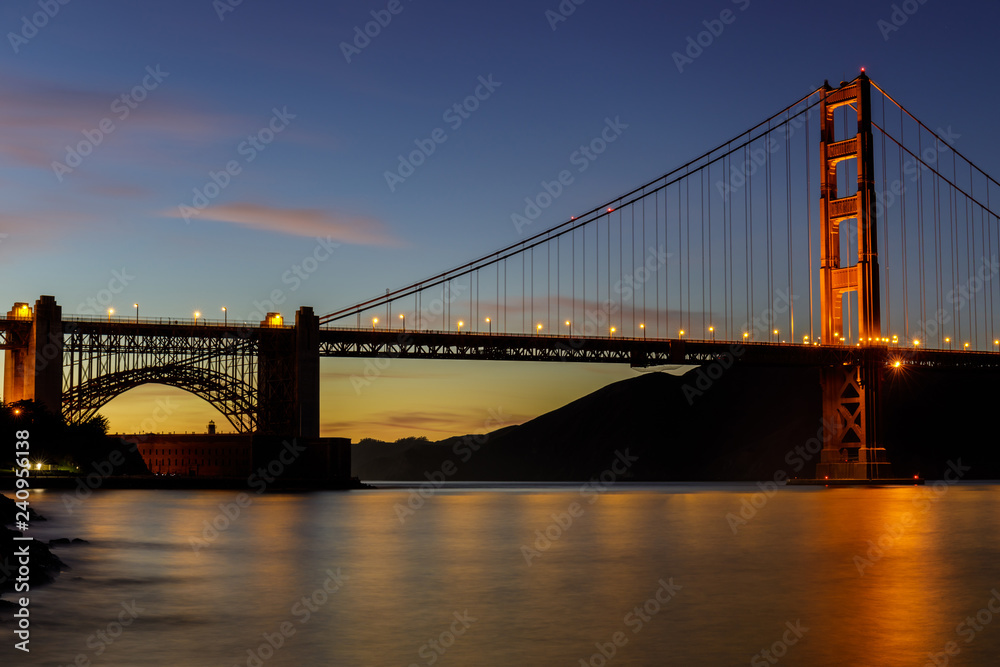 Twilight lights over the Golden Gate Bridge as seen near Fort Point Historic Site. San Francisco, California, USA.