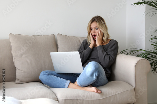 Tableau sur toile Frau sitzt auf einem Sofa und schaut erschrocken auf einen Laptop