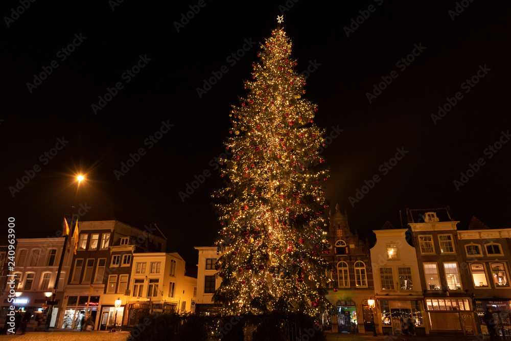 Fototapeta premium Huge lighted Christmas tree at night on the market square of Gouda with a row of medieval houses with different facades. The Netherlands, Europe.