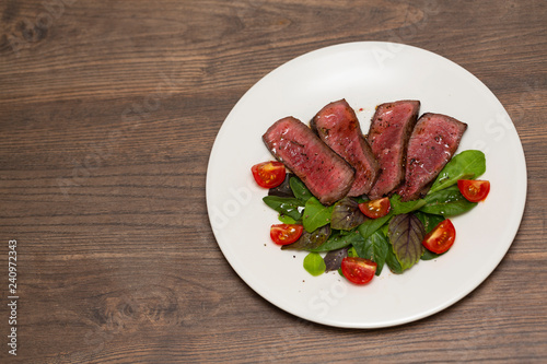 Juicy steak medium rare beef with green salad and tomatoes on white plate