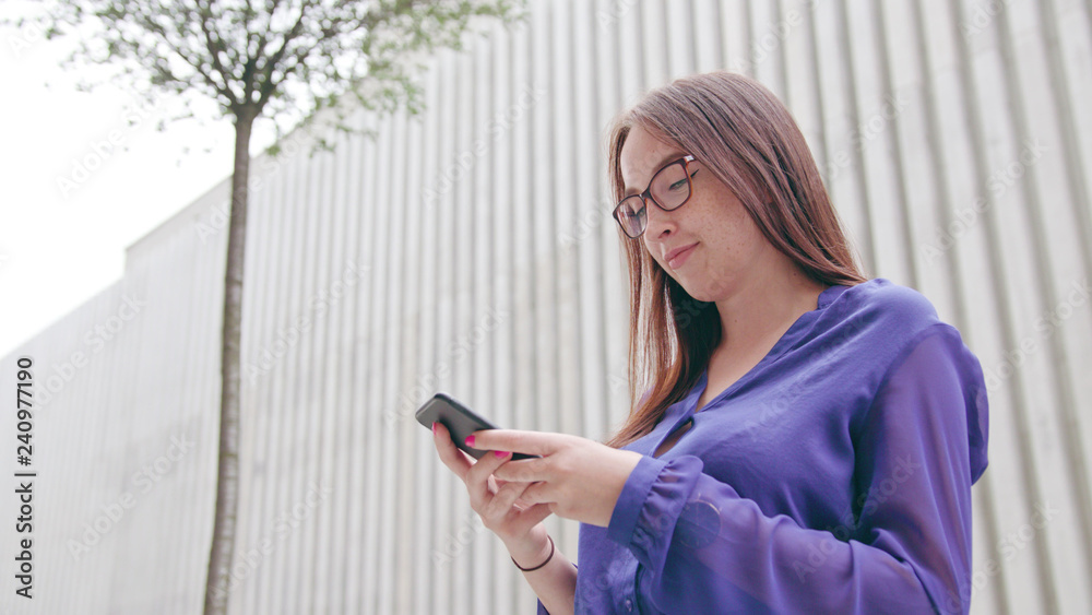 A happy smiling brunette woman with glasses using a phone in the city street. Close-up shot. Soft focus A happy smiling brunette woman with glasses using a phone in the city street. Close-up shot. Soft focus
