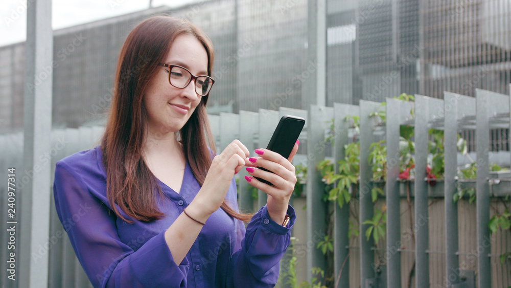A happy smiling brunette woman with glasses using a phone in the city street. Medium shot. Soft focus A happy smiling brunette woman with glasses using a phone in the city street. Medium shot. Soft focus