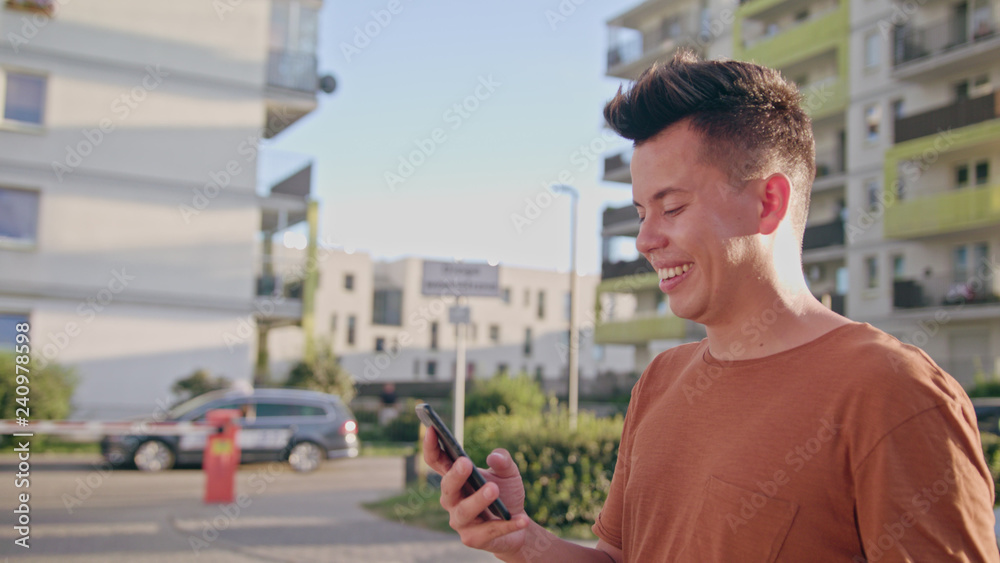 An attractive young man wearing an orange T-shirt walking and using a phone in town. Medium dolly shot. Soft focus An attractive young man wearing an orange T-shirt walking and using a phone in town. Medium dolly shot. Soft focus
