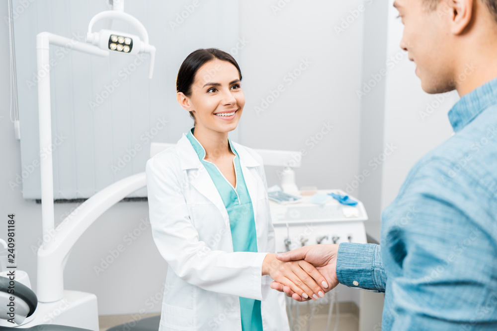 smiling female dentist shaking hands with african american patient smiling female dentist shaking hands with african american patient