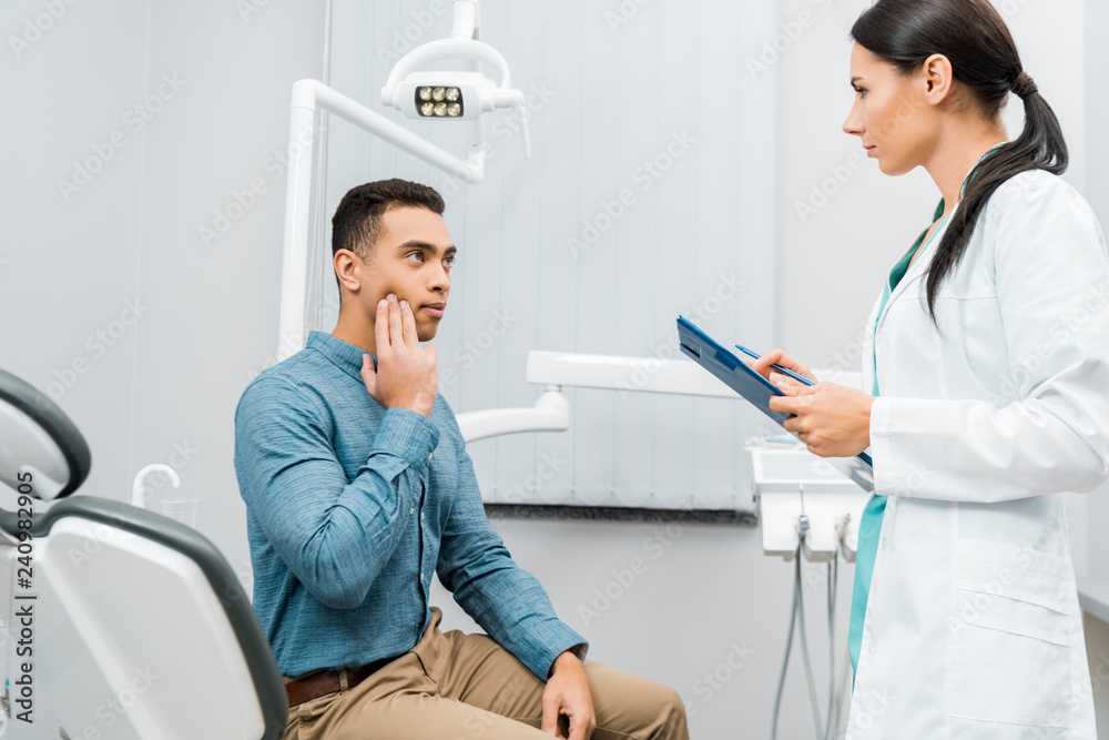 Fototapeta premium female dentist standing near african american patient with toothache