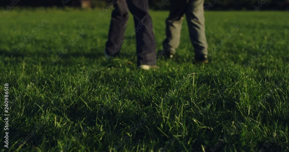 Close up of the feet of boys running on the green grass of the field and kicking a ball while playing football. Outdoors. Close up of the feet of boys running on the green grass of the field and kicking a ball while playing football. Outdoors.
