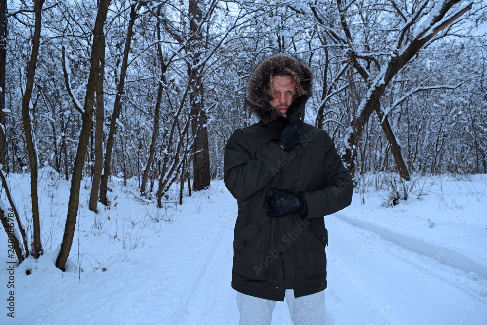 A young man in a jacket is on the road in the winter forest.