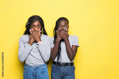 Portrait of a young two afro american surprised women standing over yellow background