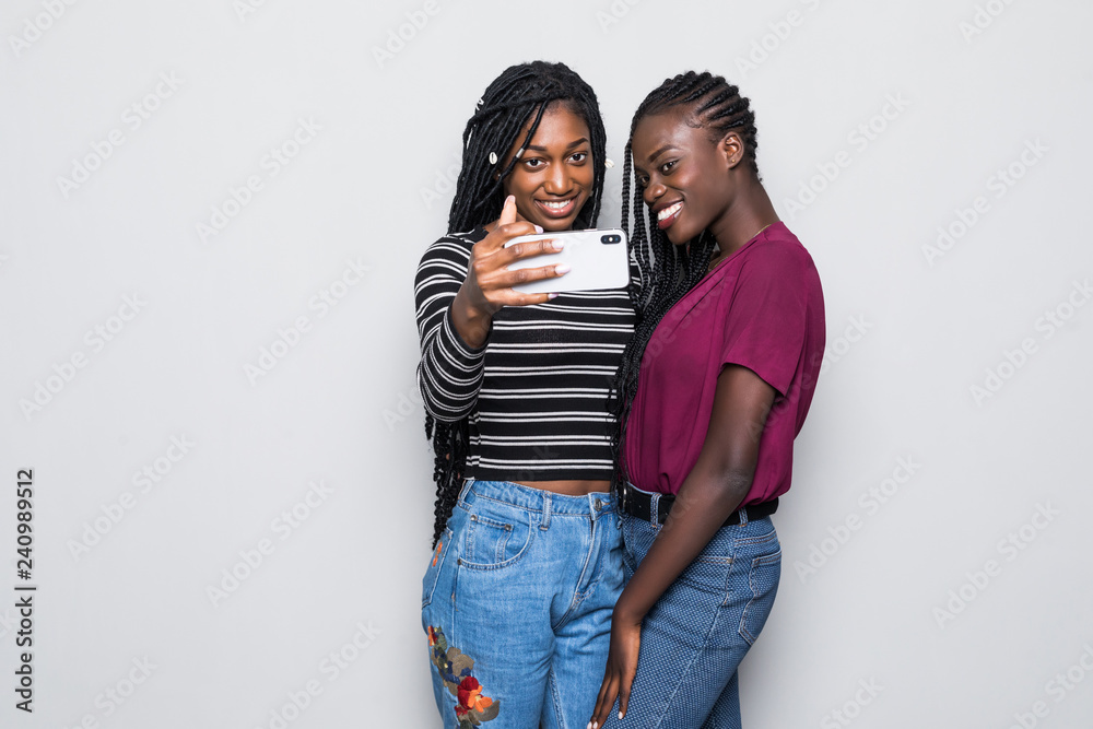 Portrait of young two african young girls taking selfie on smartphone isolated over white background
