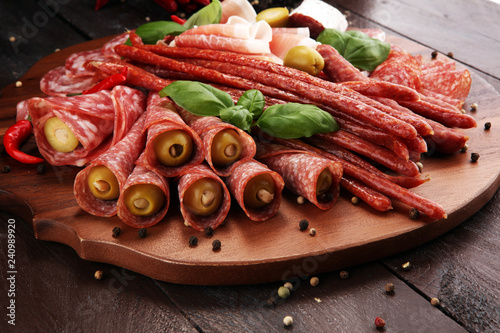 Food tray with delicious salami, pieces of sliced prosciutto crudo, sausage and basil. Meat platter with selection