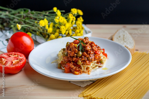 Italian spaghetti with a meat based sauce in a plain white plate on wooden table. Spaghetti pasta with tomatoes.
