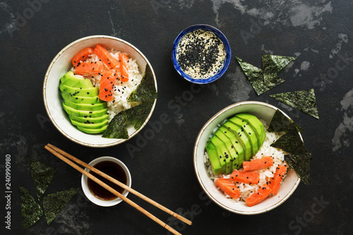 Poke bowl with salmon rice and vegetables on a dark stone background. Traditional Hawaiian raw fish salad. Top view, flat lay.