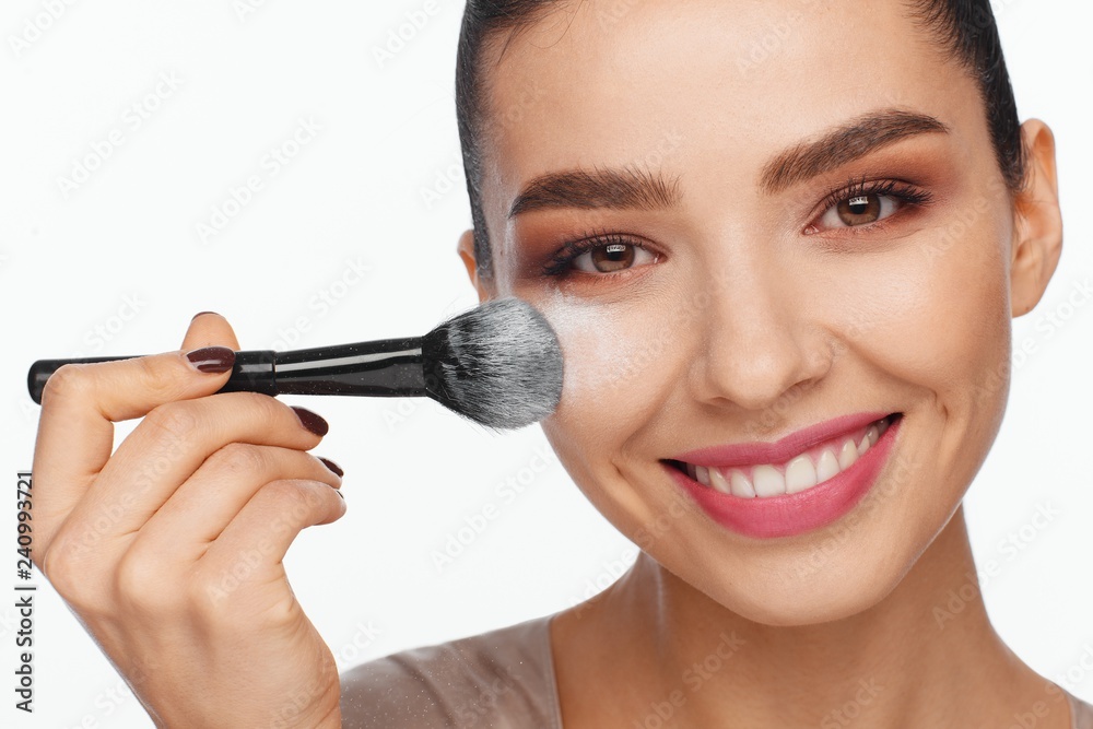 Portrait of a beautiful smiling young woman holding a brush in her hand and applying powder to her face with a brush Portrait of a beautiful smiling young woman holding a brush in her hand and applying powder to her face with a brush